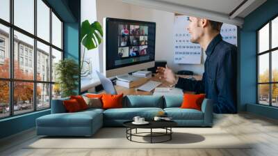 Young man having a video call via a computer in the home office. Stay at home and work from home concept during Coronavirus pandemic. Virtual house party  Wall mural