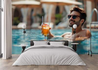  man in sunglasses enjoys a refreshing tropical cocktail while relaxing in a pool. Luxurious resort setting with lounge chairs and umbrellas in the background Wall mural