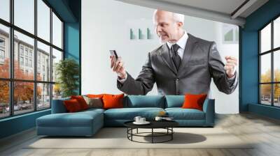 Furious senior businessman looking at smartphone screen and rais Wall mural