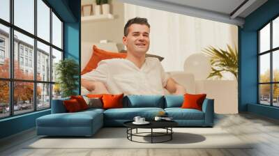 Man smiling and relaxing on couch at home Wall mural