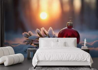 A red Christmas ornament rests on snow-covered leaves during a serene winter sunset in the forest Wall mural