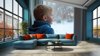 Boy in blue sweater looking at snowflakes through window. Winter scene with snowy background. Child gazing outside during wintertime. Seasonal portrait for holiday or Christmas design Wall mural