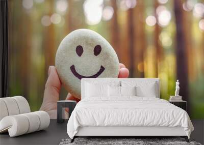 Close-up of a hand with smiling stone on forest in the background. Concept of happy life and positive thinking Wall mural