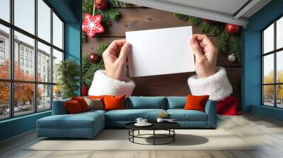 Top view of Santa's hands holding a blank card mockup on wooden background with Christmas decorations - Mockup Wall mural