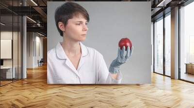 A young female doctor holds a red Apple on a gray background. the concept of proper nutrition Wall mural