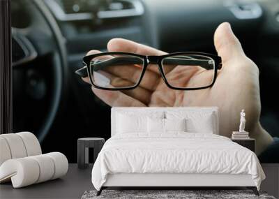 Car driver hand holding optical glasses on car interior background close up Wall mural