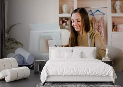 Young woman making clothes using sewing machine. Sitting at her working place at home Wall mural