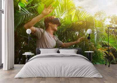 man in gray T-shirt, virtual reality 3D headset and exploring the play on a background of nature jungle Wall mural