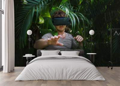 man in gray T-shirt, virtual reality 3D headset and exploring the play on a background of nature jungle Wall mural