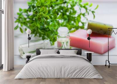 Two glass bottles with oil in it, handmade soap and green plant on a white wooden table Wall mural