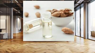 Two small glass bottles with oil inside, almond in shell on a white wooden table Wall mural