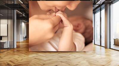 A mother kissing and holding hand the hand of her newborn baby. Wall mural