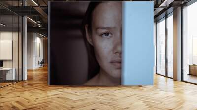 A sad face of a woman hiding behind a door afraid and terrified. Wall mural