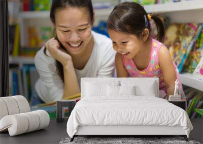 Parent and child reading books together in the library. Wall mural