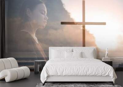 Religious woman praying to god next to a cross, peaceful nature. Wall mural