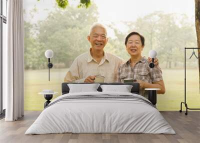 Asian elderly couple drink tea coffee in moring park sun light Wall mural