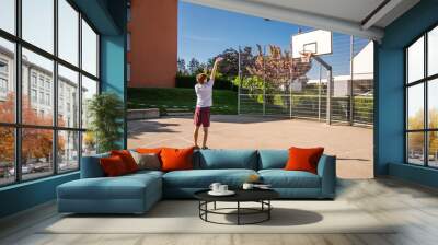 Young male basketball player playing basketball. Throwing the ball at playground. Precision shot Wall mural