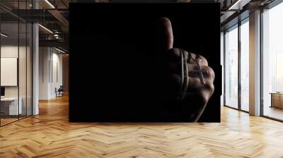 Praying with a rosary. hand of Catholic man with rosary on black background. Hands holding a silver rosary or cross pendant of Jesus Christ. Crucifix and hand on black background. Praying God concept Wall mural