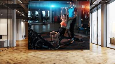 young female exercising in gym with dumbbell with personal athletic trainer Wall mural