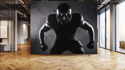 American Football Player in Shadow:  A powerful silhouette of an American football player in full gear, ready for action against a dark, smoky background. Wall mural