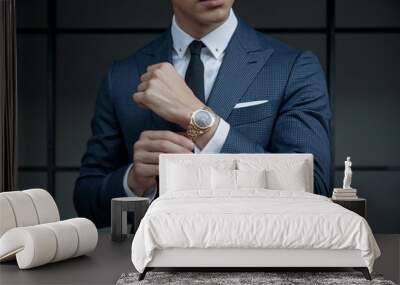 Executive Elegance: A stylish businessman adjusts his cufflinks, showcasing a luxurious gold watch and a sharp navy suit against a sophisticated dark gray background. Wall mural