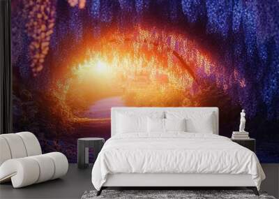 A pathway leading through a vibrant purple wisteria tunnel with a bright orange sun shining through the foliage. Wall mural