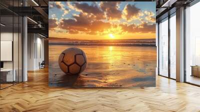 A soccer ball sits on a sandy beach with the sun setting over the ocean. Wall mural