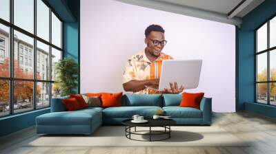 Excited young black male sitting, smiling holding using laptop in his hands Wall mural