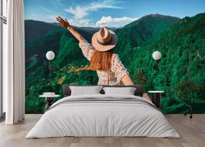 Follow me concept and traveling together. Girl traveler wearing hat, round straw bag and short jumpsuit holds the boyfriend's hand and leading to green big mountains vacation Wall mural