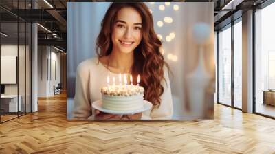 Happy contented satisfied excited laughing young woman holding birthday cake decorated with glowing candles during celebration party Wall mural