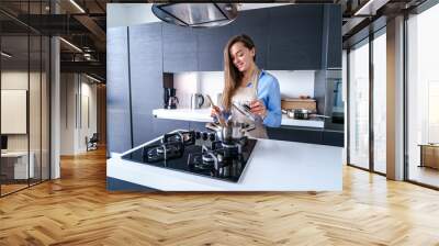 Happy smiling cooking woman housewife in apron using steel metal saucepan for preparing boiled dishes for dinner in the kitchen at home. Kitchenware for cooking Wall mural