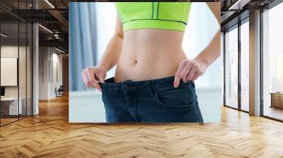 Healthy sport fitness woman with slim waist pulling her big jeans and showing weight loss and diet results. Achieving weight loss goals, motivation and progress in slimming Wall mural