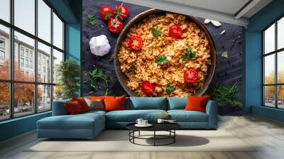 Homemade delicious pilaf with chicken, fresh parsley and ripe vegetables in a pan for lunch on a dark background. Top view Wall mural