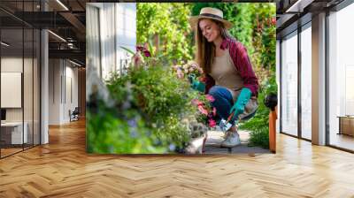 Portrait of happy gardening woman in gloves, hat and apron plants flowers on the flower bed in home garden. Gardening and floriculture. Flower care Wall mural