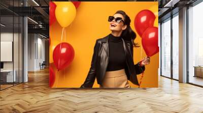 Satisfied joyful happy stylish woman holding helium colored balloons on a yellow background, congratulations on the holiday day Wall mural