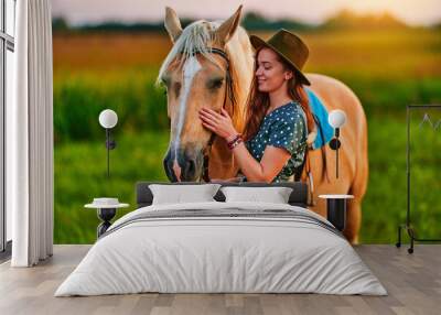 Young cute happy joyful satisfied smiling woman hugging and stroking beautiful blond palomino horse at meadow at sunset Wall mural