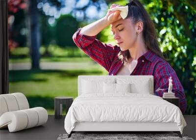 Young unhappy tired woman with cold refreshing water suffering from hot weather while walking in a park Wall mural