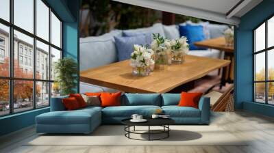 Vases with bouquets of white flowers on the table with blue couch on the background Wall mural