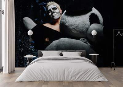 halloween make up. scary man ready for party.strange male with skull painted on his face plays with creepy huge panda toy in black Studio alone Wall mural