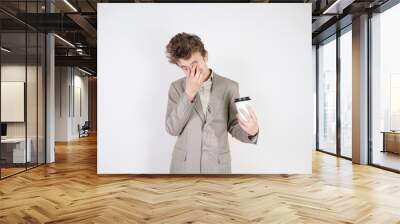 tired teen boy in grey business suit with paper Cup of coffee in hand on white studio background Wall mural