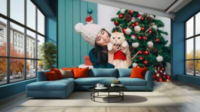 Portrait of young woman and cute cat wearing sweater. christmas tree and presents background Wall mural