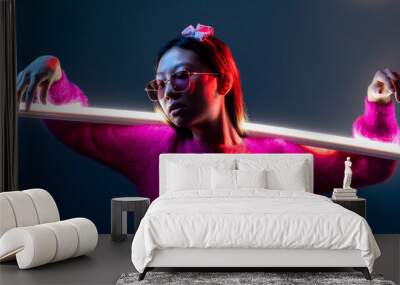 Cyberpunk fashion. Neon light people. Futuristic portrait. Glamour Asian girl in pink in sunglasses in red color glow with illuminated white LED lamp stick isolated on dark night blue. Wall mural