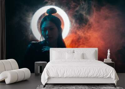 Cyberpunk fashion. Night portrait. Futuristic beauty. Blue neon light Asian girl in black leather jacket with white glowing halo in red color smoke on dark copy space background. Wall mural