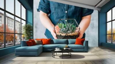 DIY florarium. Handmade natural gift delivery service. Cropped shot of woman holding glass geometric vase with succulents. Wall mural