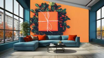 Floral art and craft ideas. Top view of handmade gift box with rose hip berries and green leaves on orange background. Copy space. Wall mural