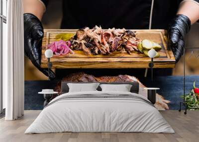 Grill restaurant kitchen. Chef hands in black cooking gloves holding smoked pulled pork with pickles on wooden board. Wall mural