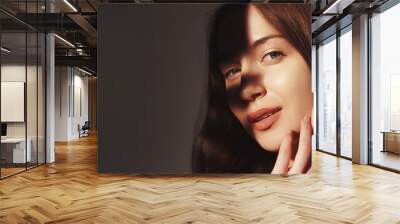 Hydrated skin. Care procedure. Cosmetics advertising. Beautiful gentle young woman touching perfect radiant clear face with shadow isolated on beige empty space. Wall mural