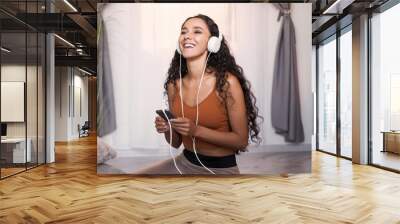 Music inspiration. Sound pleasure. Happy smiling girl in headphones enjoying listening to audio on phone at light modern home interior with copy space. Wall mural