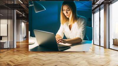 Night work. Remote job. Freelancer lifestyle. Late task. Serious smart workaholic woman using laptop typing at dark workplace with desk lamp light in home office. Wall mural