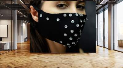 Pandemic fashion. DIY accessory. Quarantine festive look. Closeup portrait of mysterious woman in black glamour reusable handmade fabric face mask with rhinestone decor on dark background. Wall mural